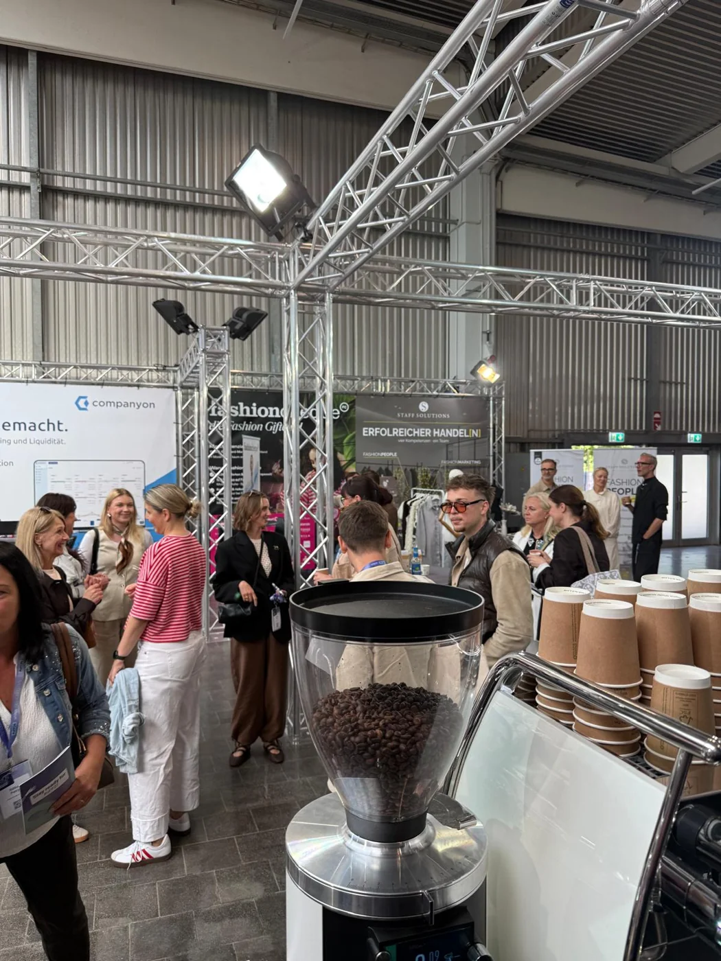 Blick von der Kaffeebar auf Messebesucher im Gespräch zwischen Ausstellungsständen